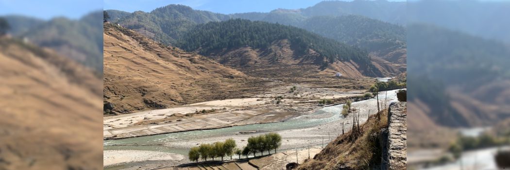 A river running through a valley with tree lined mountains behind.