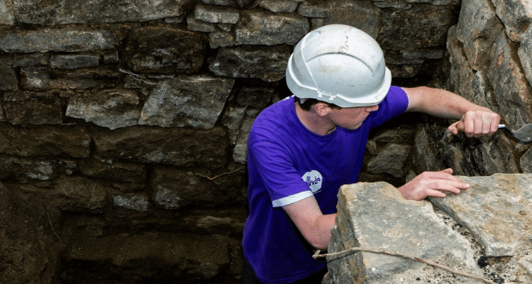 Archaeology student wearing a hard hat at a dig site