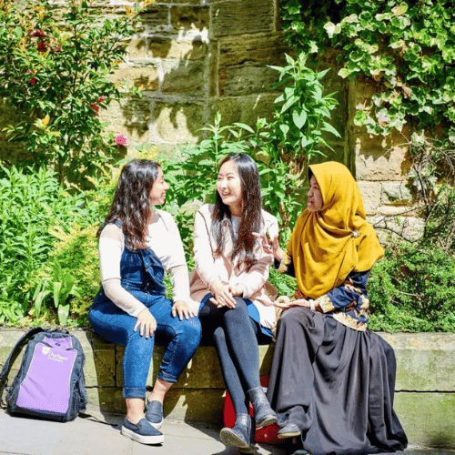 Three Durham students outside sat on a stone wall talking