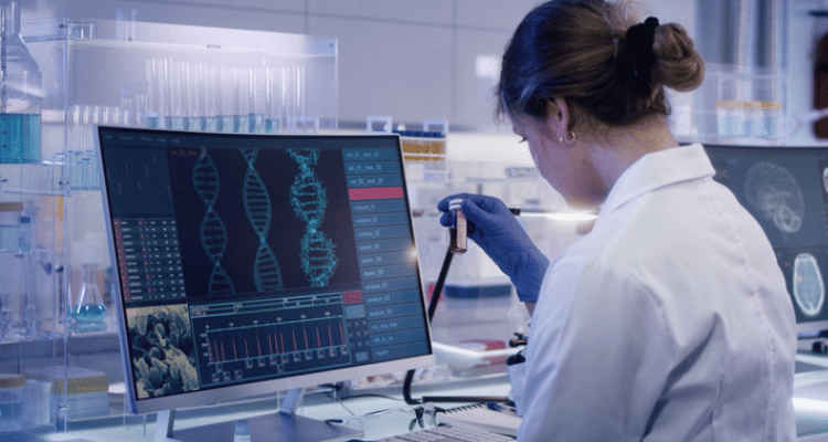 Student sat in a research lab using a pipette and petri dish with a computer screen